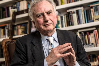 Richard Dawkins sitting on a chair with a bookshelf in the background.