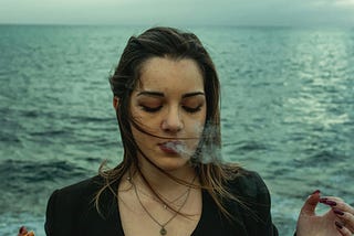 woman smokes in front of ocean