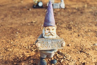 A garden gnome in a barren yard, holding a sign that says “Go away.”