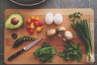 A large cutting board with fresh vegetables and a knife.