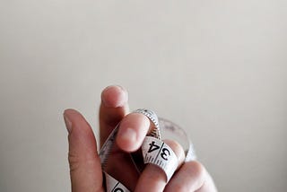 A hand with an inch tape tangled around the fingers on a white background.