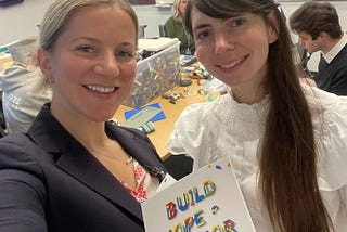 Two women holding a “build hope for Ukraine” sign with LEGO bricks in the back