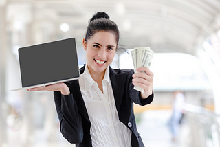 Woman with a big smile, holding a fist full of money, and a laptop.