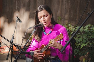 a woman — the author — plays ukulele and sings into microphones outside