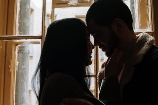 man and woman kissing near window