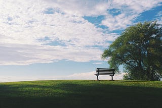 A bench at the crest of a hill with a cloudy sky above.