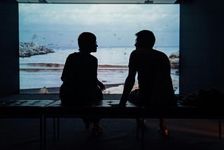 A silhouette of a girl and a boy looking at each other while sitting on an ottoman