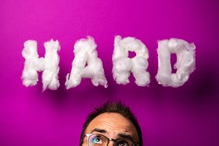 Bearded man wearing glasses, puzzled and concerned, staring up at the word “HARD”
