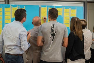 People standing around a whiteboard with sticky-notes on it, looking busy