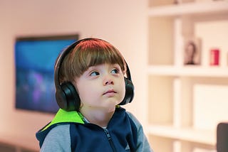 A hella cute child with black headphones on and looking sideways. Probably looking at the adults acting out.