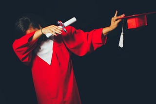 A person in a red graduation gown dabbing with a diploma and cap in their hands.