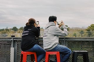 Two people using smartphones. One person is using it in portrait position and another in landscape position.