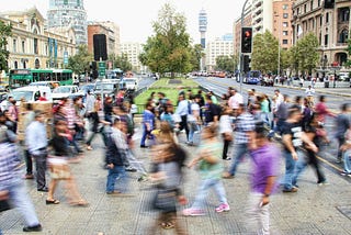 A city street with a lot of people crossing the street, blurred to create a sense of motion and activity