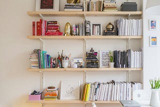bookshelves arranged with stacks of books, pencil cup full of pens and pencils and some frames