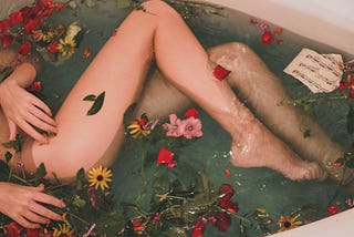 A woman with beautiful legs soaks in a tub with flowers.