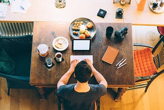 Man types on an iPad on his desk while surrounded by food.