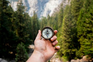 A hand holding a compass in a forest, symbolizing finding direction in life and taking small steps toward a larger goal.