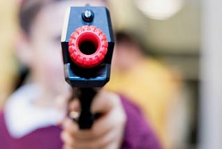 close up of toy gun barrel with out of focus child holding the gun handle