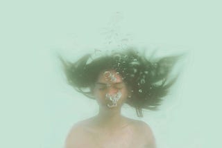 A woman underwater, blowing air from her mouth. Her hair is floating upwards.