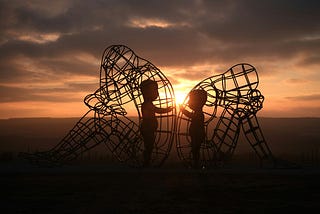 Burning Man: Two figures connecting behind two figures with their backs turned.