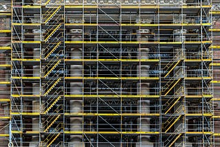 Dense metal scaffolding wrapped around a historic stone building, forming a temporary load-bearing structure that supports work under pressure while the underlying architecture remains unchanged.
