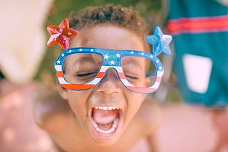 A child in patrotic glasses screaming with their mouth open