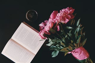 An open book on a table, with a cup of coffee and a bouquet of flowers.