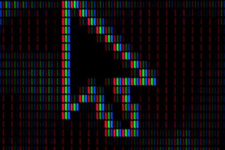 Close-up of a computer cursor arrow formed by RGB pixel strips against a dark background, showing the individual red, green, and blue elements that make up a digital display.