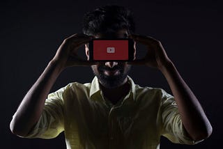Man hiding his face behind a phone with a red screen and white ‘play’ button.