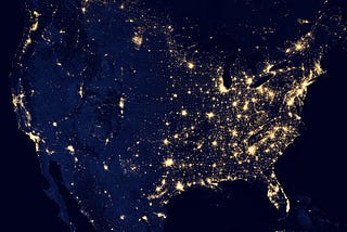 An aerial shot of the United States, showing the most populated areas lit up by lights.