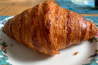A golden brown crispy croissant on a china plate