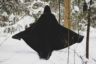 figure walking away in the snow in a black cloak