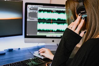 woman in headphones sits at desk working in a digital audio interface on her computer
