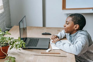 Young boy watching a video call on a laptop with a paper and pencil in front of him