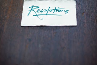 A small rectangular piece of paper with “resolutions” written on it placed on a table.