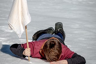 Man face down in the sand, holding a white flag