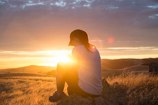 A woman sits within the rays of a sunset.