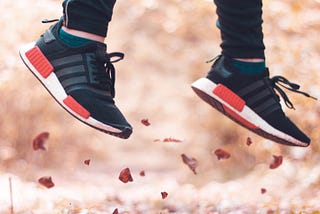 Sneaker-clad feet and lower leg shown jumping up from leaf-strewn ground