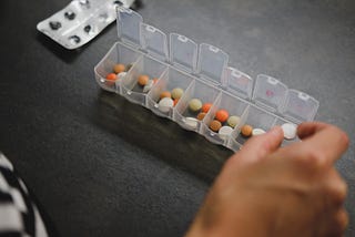 photo of a hand placing a pill into a plastic weekly pill organizer.