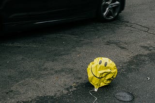 smiley face deflated balloon on the side of a road