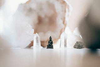 In the midst of clear crystals and geodes sits a black ebony statue of a person meditating, sitting cross legged and erect.