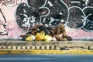Homeless man lying on the sidewalk among his bags