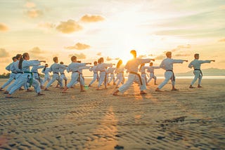 Various individuals performing a Kata on a beach.