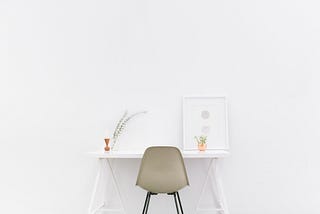 A bare white room with a white desk and beige office chair.