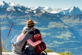 Hikers in an embrace, looking out at snow-topped mountains.