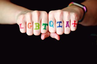 A photo of LGBTQIA+ written in rainbow-colored letters across someone’s knuckles