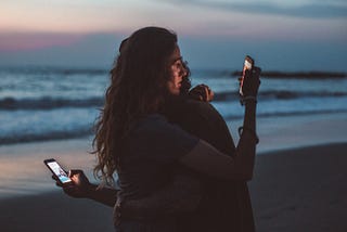 couple hugging and using smartphone near sea on sunset
