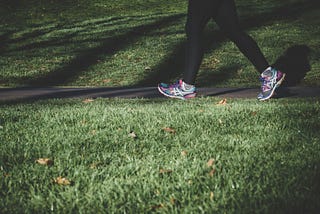 A person walking along a pathway. Only their legs are on view. They are wearing trainers and black leggings. There is grass in the foreground.