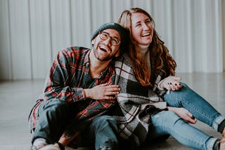 A guy and a girl are laughing with each other while sitting on the ground.