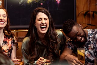 Two women and a man are laughing out loud. They are having a great time together, drinking from their glasses.